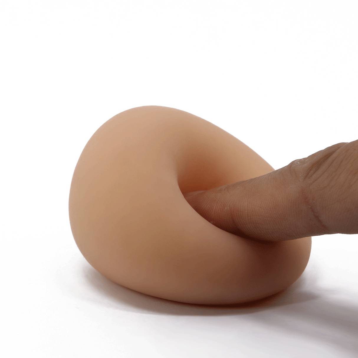 A finger presses into the soft, flesh-toned TPR material of a compact, egg-shaped male masturbator.